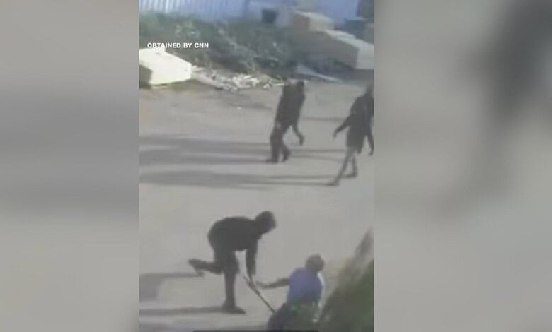 Image shows a masked man with a stick beating a man in a blue shirt