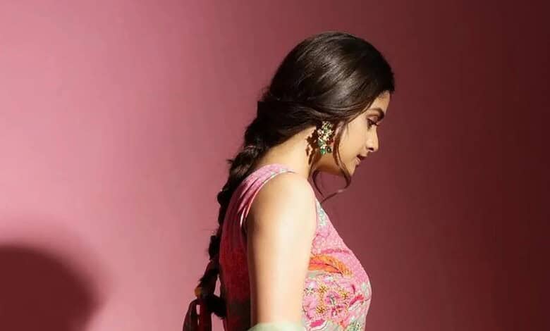 Woman in traditional dress with braided hair, looking down against pink backdrop.