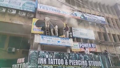 Workers cleaning smoke damage on a multi-storey building with advertising banners and signs.