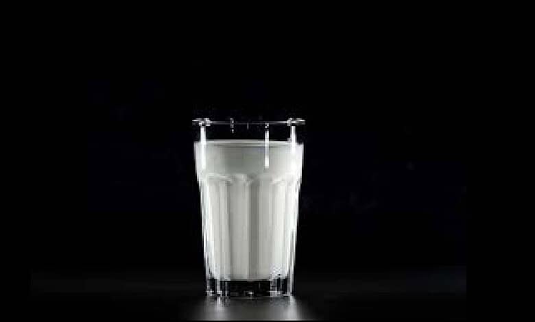 Glass of milk with a metal clamp on a dark background.