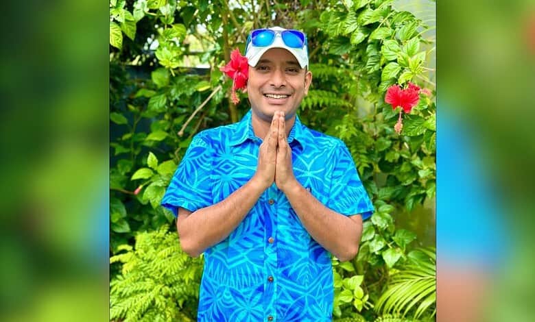 Anvesh smiling outdoors wearing sunglasses, surrounded by tropical plants and flowers.