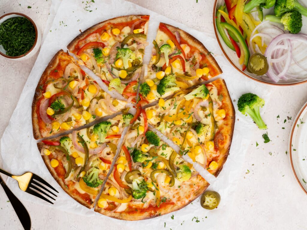 Vegetarian vegetable pizza with peppers, broccoli, and corn, served with a side salad.