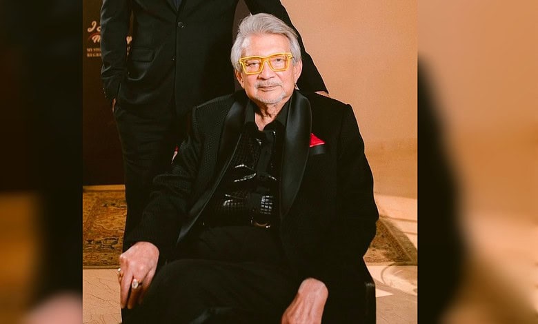 Rajan Lall in black suit with yellow glasses seated indoors at an event.