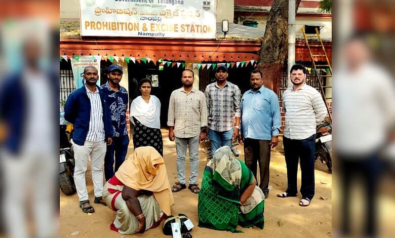 Image shows Two women crouching with heads covered in front of officers at the Nampally Prohibition & Excise Station, Telangana.
