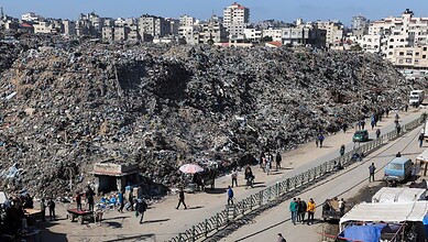 Large garbage dump in Gaza with residents walking along the street.