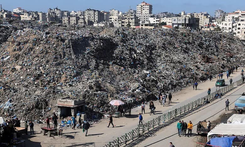 Large garbage dump in Gaza with residents walking along the street.