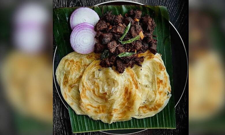 Delicious spicy beef served with crispy paratha and fresh onion slices on a banana leaf. Traditional Indi.