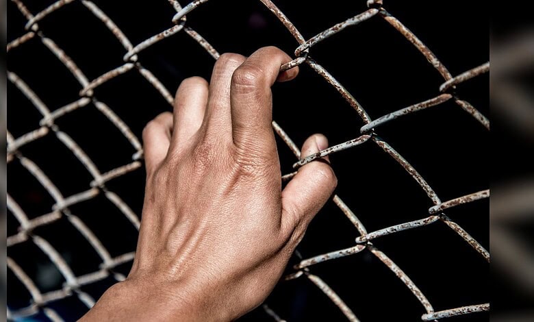 Hand gripping rusty wire fence, symbolising imprisonment or restriction.
