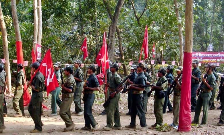 Image shows Armed Maoist insurgents in military-style uniforms carrying red flags march through a forested area during a gathering.