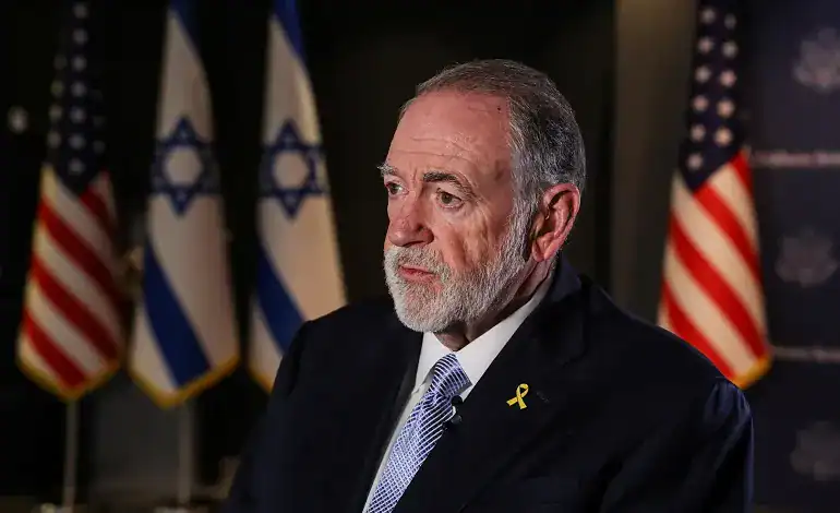 US Ambassador to Israel Mike Huckabee speaks during an interview, with Israeli and US flags in the background.