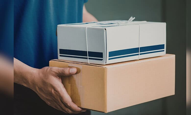 Person holding two parcels, one in a cardboard box and one in a white box, related to rail parcel service.