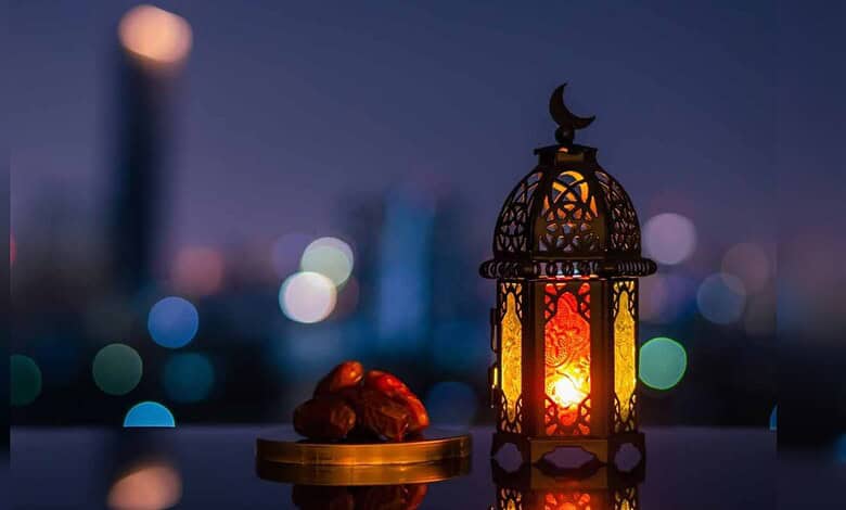 Lantern with intricate design and glowing light, placed beside dates on a balcony at dusk.