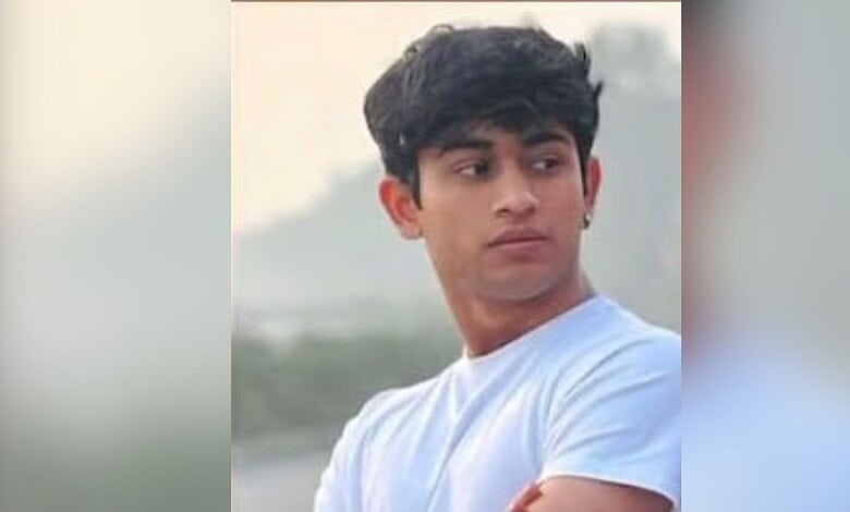 Young man with black hair in a white t-shirt looking away outdoors.