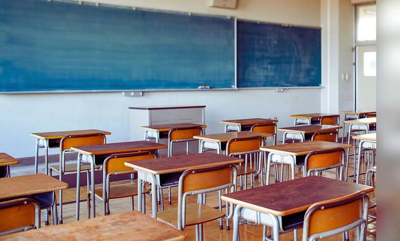 Image shows Empty classroom with wooden desks and blue chalkboards