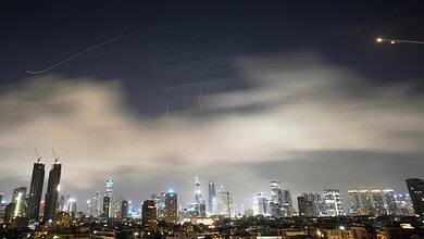 Night city skyline with tall buildings and aircraft trails in the sky.