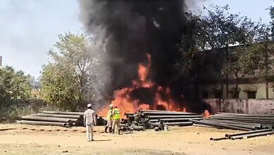Fire and smoke at construction site with workers and onlookers nearby.