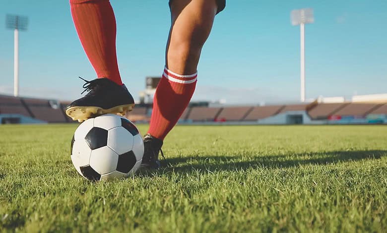 Close-up of soccer players' legs and a ball on the field, with stadium in background, during match postpo.