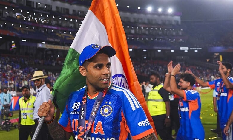 Suryakumar Yadav holding the Indian flag after a cricket match victory, surrounded by teammates and fans.