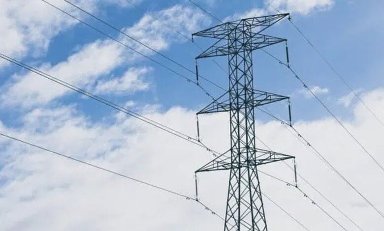 Power transmission tower with high-voltage lines against a blue sky with clouds.