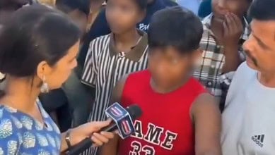 Young boy in red shirt speaking passionately to media surrounded by adults and children.