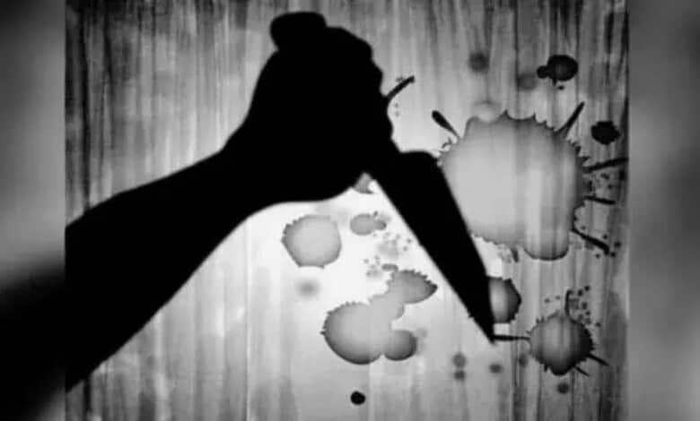 Silhouette of a hand holding a knife with ink splatters on a wooden background.