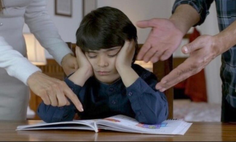 Representative image of a child covering ears while adults point at a book, appearing stressed during study.