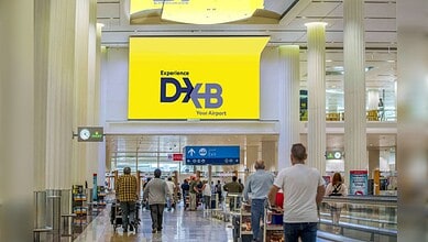 Passengers walking through Dubai International Airport terminal with DXB signage in bright yellow.