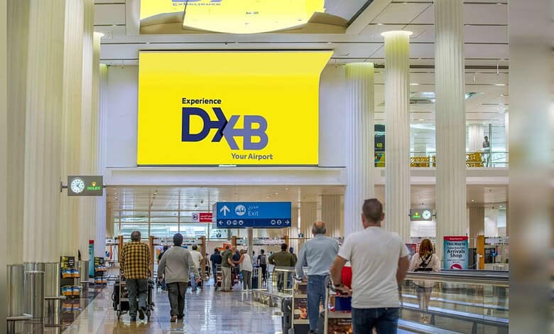 Passengers walking through Dubai International Airport terminal with DXB signage in bright yellow.