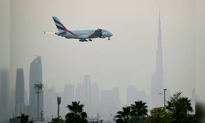 Emirates Airbus A380 approaching landing at Dubai International Airport with Dubai skyline and Burj Khalifa in the background.