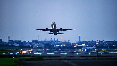 Airplane taking off from runway at dusk, with city skyline in background.