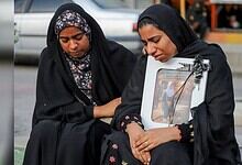 Two Iranian women mourning, holding a framed photo of schoolgirls, reflecting tragedy and loss.