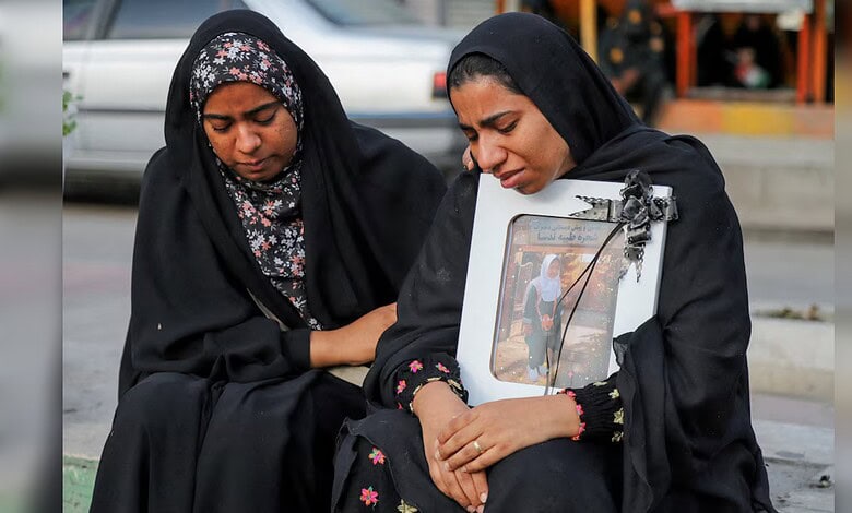 Two Iranian women mourning, holding a framed photo of schoolgirls, reflecting tragedy and loss.
