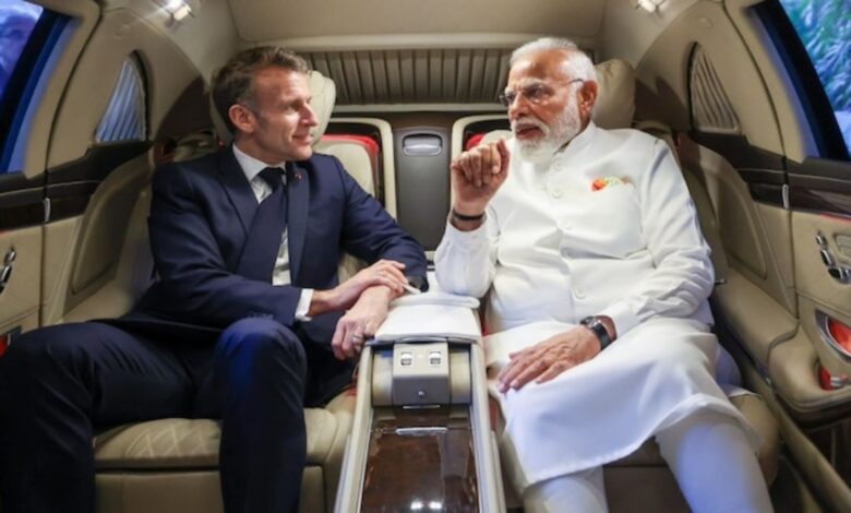 Indian Prime Minister Narendra Modi and French President Emmanuel Macron seated inside an car, engaged in conversation.