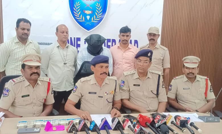 Arrested man in Hyderabad for Rs 10L bank loan fraud, surrounded by police officers during a press confer.