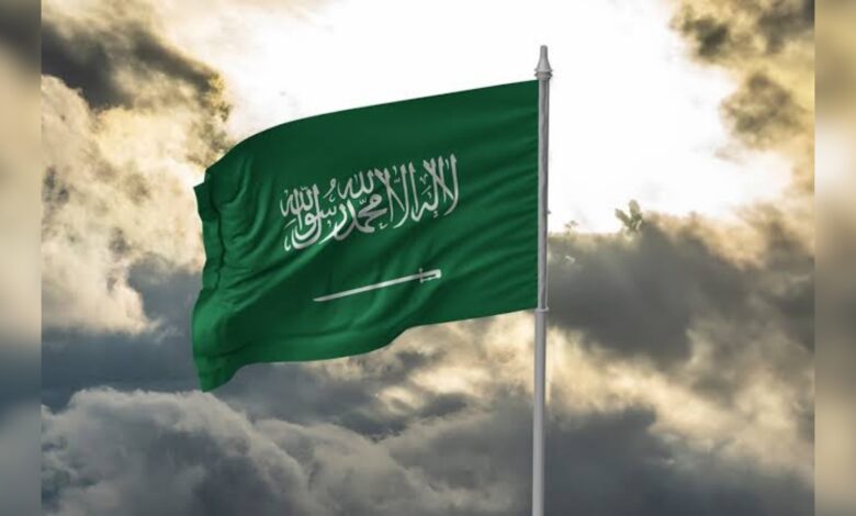 Saudi Arabian flag waving against a cloudy sky.