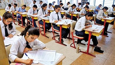 Students sit in a classroom writing board examinations at their desks.