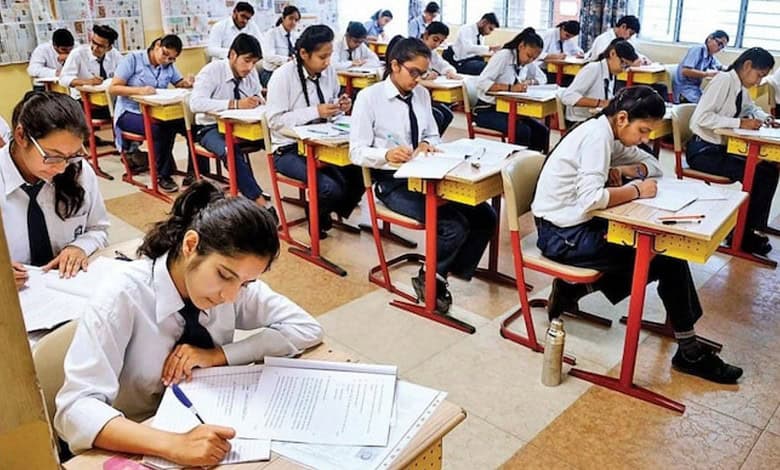 Students sit in a classroom writing board examinations at their desks.