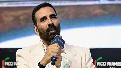 Akshay Kumar speaking into a microphone at a film event, discussing his role in Vanga and Dhar films.