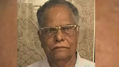 Close-up of an elderly Indian man wearing glasses and a striped shirt.