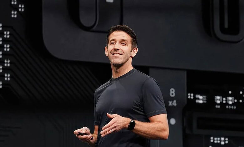 An enthusiastic male speaker presenting at a tech conference, holding a remote control, with a digital ba.