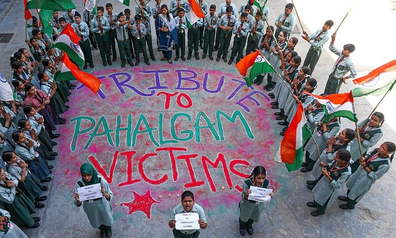 A large group of students and community members gather in a circle holding flags and signs, paying tribute to Pahalgam attack victims.