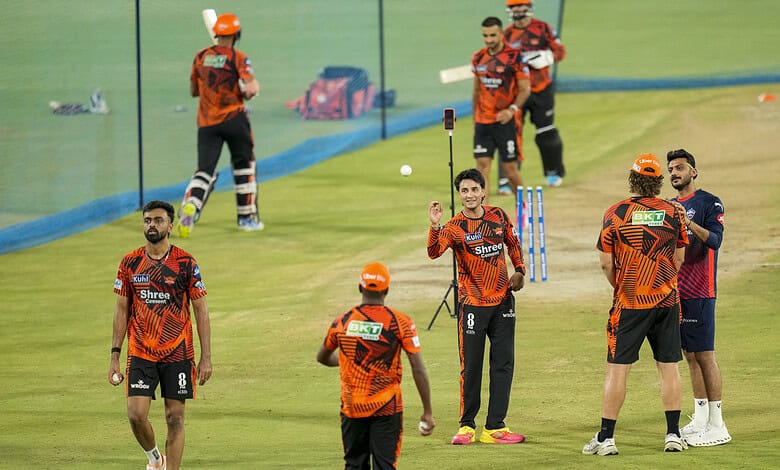 Cricket players in Hyderabad IPL match practice, wearing orange jerseys, preparing on the field amid weat.