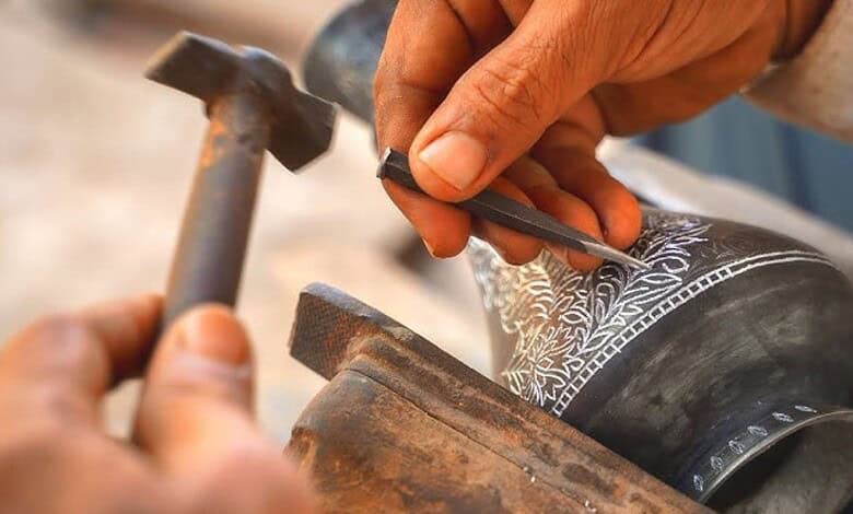 Close-up of artisan carving intricate designs on Bidriware metal vessel.