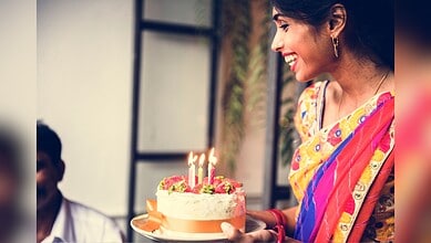 A woman in colourful traditional attire holding a birthday cake with lit candles, smiling joyfully during.