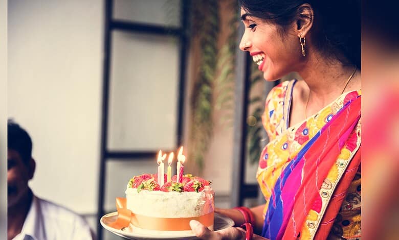 A woman in colourful traditional attire holding a birthday cake with lit candles, smiling joyfully during.