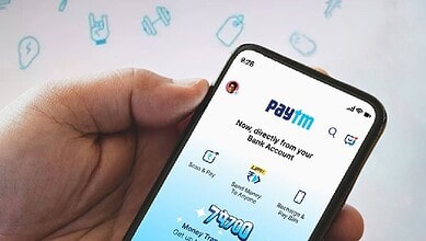 Close-up of a hand holding a smartphone displaying the Paytm app with banking options.