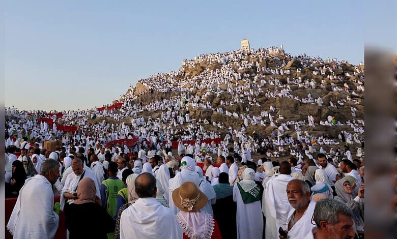 Pilgrims in white Ihram clothing gather at a hilltop during Hajj pilgrimage.