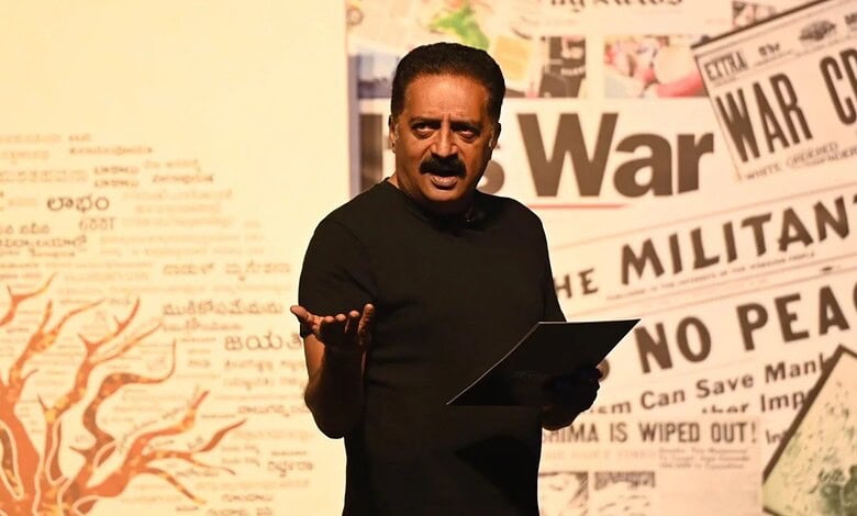 Indian man speaking at a press conference with newspaper headlines in the background.