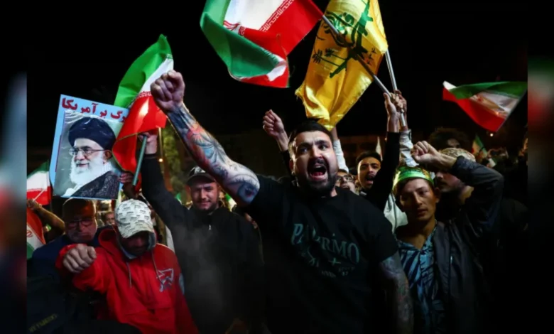 Protesters waving Iranian and Hezbollah flags and holding a portrait of Ayatollah Ali Khamenei during a night-time rally.