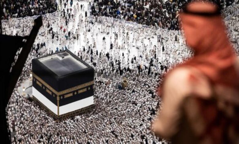 Muslim pilgrims gathered around the Kaaba at the Grand Mosque in Makkah, with a blurred figure in the foreground.